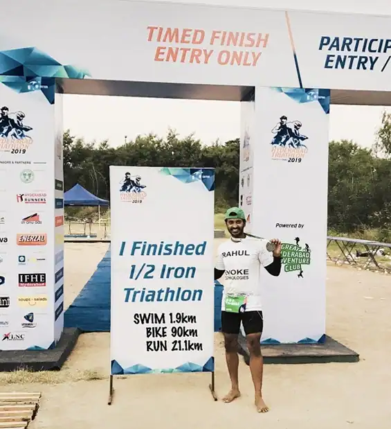 Triathlete celebrating at the finish gate holding a board that reads ‘I Finished 1/2 Iron Triathlon’
